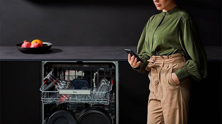 Kvinna i grönt använder mobiltelefon framför diskmaskin