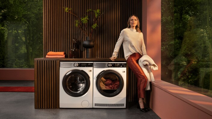 En kvinna står och väntar vid en torktumlare på att tvätten ska bli torr.