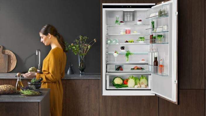 En kvinna tar ut livsmedel ur ett kylskåp som står med dörren full öppen.