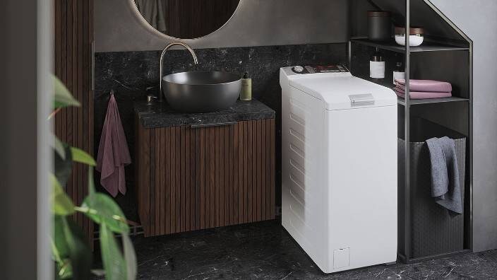 En toppmatad tvättmaskin stående i ett mindre tvättutrymme.
