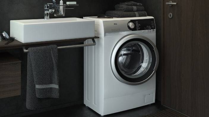 En kompakt tvättmaskin står placerad i ett mindre badrum.