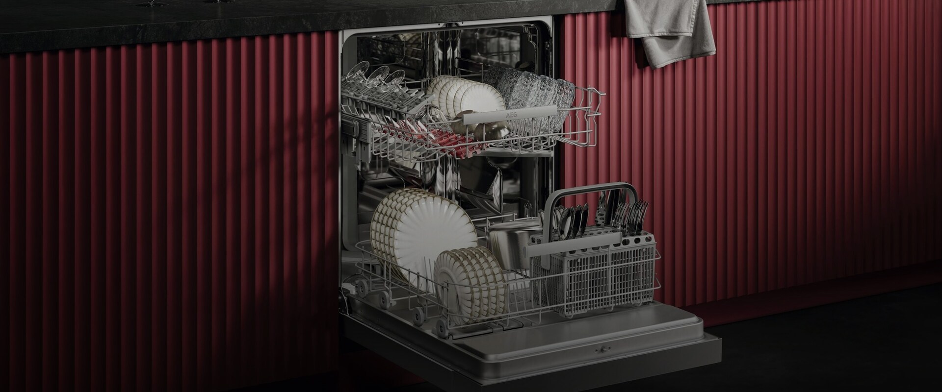 Öppen AEG-diskmaskin i en modern röd köksmiljö som visar rymlig korgförvaring för tallrikar, glas och bestick.