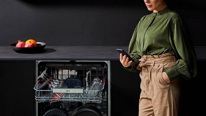 Öppen diskmaskin och kvinna som kollar i telefonen